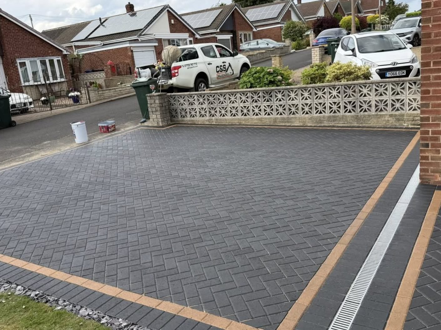 Charcoal herringbone block paved driveway with a buff contrasting border and channel drain