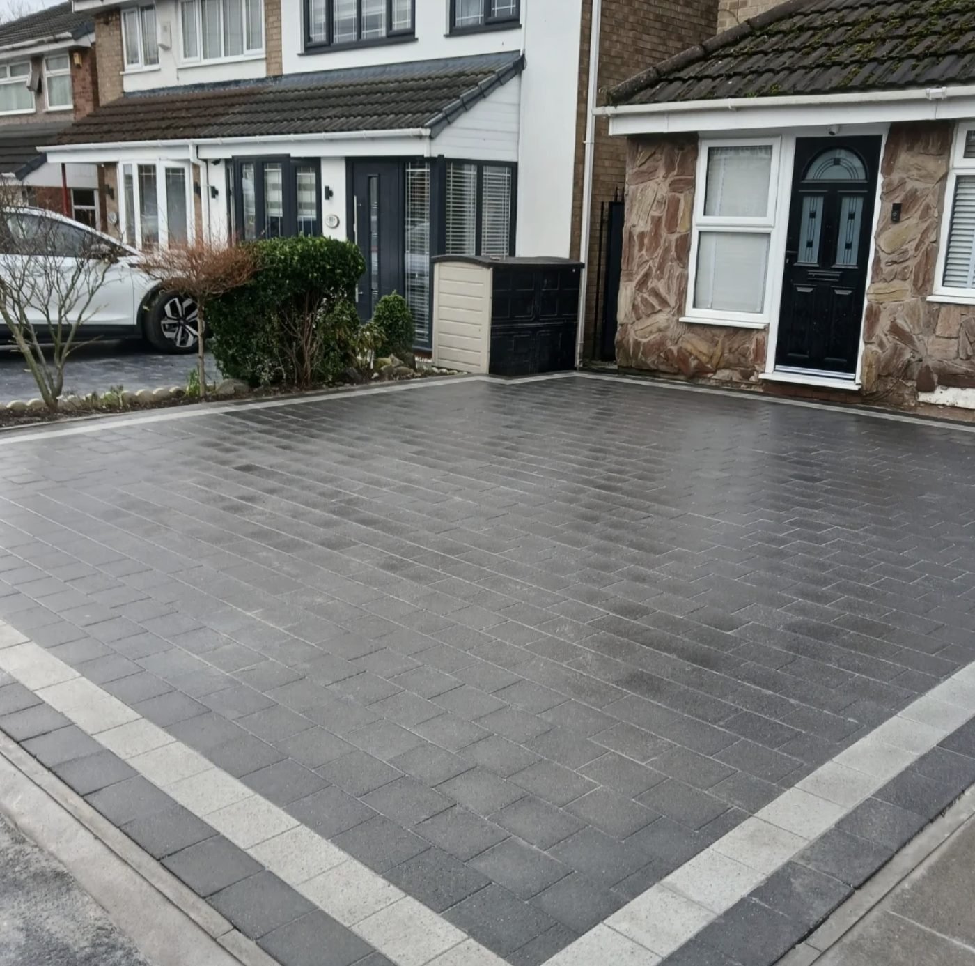 Charcoal block paved driveway framed by a light silver double border